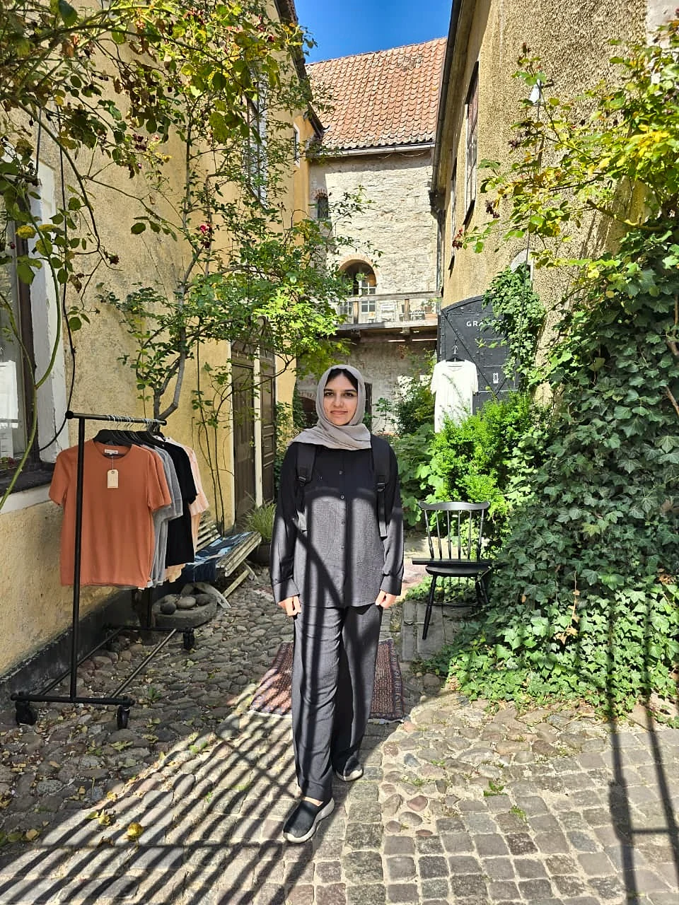 Arwa in a sunny cobbled alley with ivy-covered stone walls.