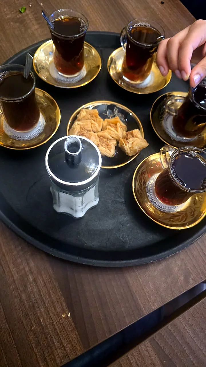 A tray of Turkish tea glasses and sweets on a wooden table.